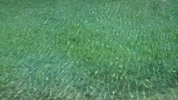 Turkos havsvatten genomsyras av solstrålar. Krusningar i vattnet från vinden. Blått klart vatten. Vågor och genomskinlig sandbotten. — Stockvideo