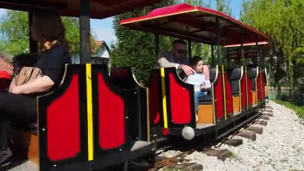 Στανισίτσι, Μπιελίνα, Β-Ε, 25 Απριλίου 2021. Μια παιδική ατμομηχανή με ανθρώπους και παιδιά οδηγεί επιβάτες. Η ατμομηχανή και οι άμαξες είναι βαμμένες κόκκινες. Θερινό πάρκο διασκέδασης. Σιδηροδρομικό παιχνίδι — Αρχείο Βίντεο