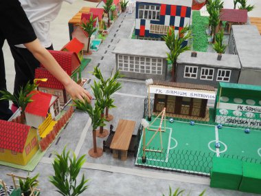 Siyah elbiseli bir çocuk kağıt bir modelle masaya uzanır. Bir şehir ya da bölgenin modelidir. Okul ödevi sokağınızı resmetmek için. Okulda çalışma dersi ya da proje