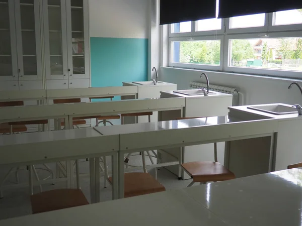 Chemistry room in a modern new school. Beautiful white furniture with sinks and washbasins. Large windows with blackout curtains or blinds. Empty school classroom. Furniture and school equipment.