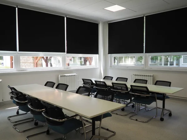 table and chairs in the meeting room in the office, in the classroom or in the library hall. White, black and gray paints in the interior. Black blinds for darkening the room. Modern interior design.