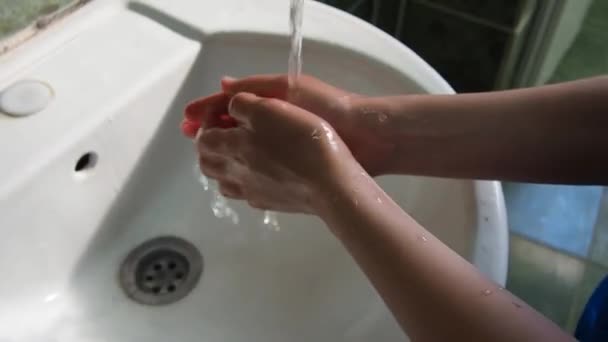 Un niño de 8 años se lava las manos sobre el fregadero. Las manos de los niños bajo un chorro de agua limpia que fluye del grifo. Higiene y prevención de enfermedades infecciosas. Cuarto de baño o aseo público. — Vídeo de stock