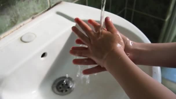 Восьмилетний мальчик моет руки над раковиной. Детские руки под потоком чистой воды, текущей из-под крана. Гигиена и профилактика инфекционных заболеваний. Ванная или общественный туалет. — стоковое видео