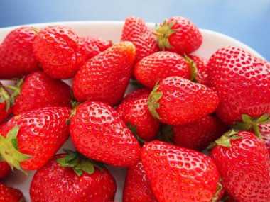 Tabakta çilek, mavi arka plan. Beyaz tabaklar ve olgun kırmızı büyük bahçe çilekleri. Sağlıklı yiyecekler, vitaminler ve vejetaryen diyeti. Yiyeceklerle yaşam. Uzayı kopyala Düz yatıyordu.