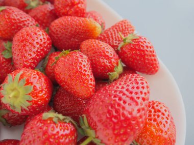 Tabakta çilek, beyaz arka plan. Beyaz tabaklar ve lezzetli kırmızı büyük bahçe çilekleri. Sağlıklı yiyecekler, vitaminler ve vejetaryen diyeti. Yiyeceklerle yaşam. Uzayı kopyala Düz yatıyordu.