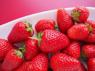 Tabakta çilek, pembe arka plan. Beyaz tabaklar ve olgun kırmızı büyük bahçe çilekleri. Sağlıklı yiyecekler, vitaminler ve vejetaryen diyeti. Yiyeceklerle yaşam. Uzayı kopyala Düz yatıyordu.