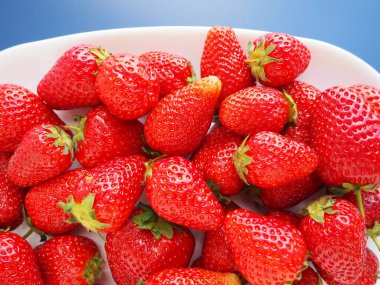 Tabakta çilek, mavi arka plan. Beyaz tabaklar ve olgun kırmızı büyük bahçe çilekleri. Sağlıklı yiyecekler, vitaminler ve vejetaryen diyeti. Yiyeceklerle yaşam. Uzayı kopyala Düz yatıyordu.