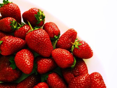 Tabakta çilek, beyaz arka plan. Beyaz tabaklar ve lezzetli kırmızı büyük bahçe çilekleri. Sağlıklı yiyecekler, vitaminler ve vejetaryen diyeti. Yiyeceklerle yaşam. Uzayı kopyala Düz yatıyordu.