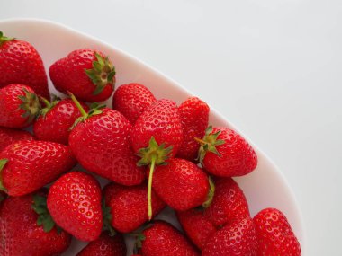 Tabakta çilek, beyaz arka plan. Beyaz tabaklar ve lezzetli kırmızı büyük bahçe çilekleri. Sağlıklı yiyecekler, vitaminler ve vejetaryen diyeti. Yiyeceklerle yaşam. Uzayı kopyala Düz yatıyordu.