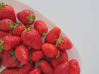 Tabakta çilek, beyaz arka plan. Beyaz tabaklar ve lezzetli kırmızı büyük bahçe çilekleri. Sağlıklı yiyecekler, vitaminler ve vejetaryen diyeti. Yiyeceklerle yaşam. Uzayı kopyala Düz yatıyordu.