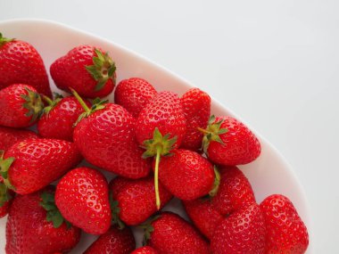 Tabakta çilek, beyaz arka plan. Beyaz tabaklar ve lezzetli kırmızı büyük bahçe çilekleri. Sağlıklı yiyecekler, vitaminler ve vejetaryen diyeti. Yiyeceklerle yaşam. Uzayı kopyala Düz yatıyordu.