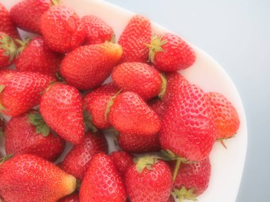 Tabakta çilek, gri arka plan. Beyaz tabaklar ve lezzetli kırmızı büyük bahçe çilekleri. Sağlıklı yiyecekler, vitaminler ve vejetaryen diyeti. Yiyeceklerle yaşam. Uzayı kopyala Düz yatıyordu.