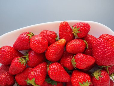 Tabakta çilek, gri arka plan. Beyaz tabaklar ve lezzetli kırmızı büyük bahçe çilekleri. Sağlıklı yiyecekler, vitaminler ve vejetaryen diyeti. Yiyeceklerle yaşam. Uzayı kopyala Düz yatıyordu.