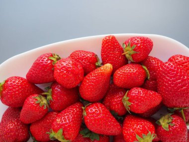 Tabakta çilek, gri arka plan. Beyaz tabaklar ve lezzetli kırmızı büyük bahçe çilekleri. Sağlıklı yiyecekler, vitaminler ve vejetaryen diyeti. Yiyeceklerle yaşam. Uzayı kopyala Düz yatıyordu.