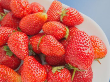 Tabakta çilek, gri arka plan. Beyaz tabaklar ve lezzetli kırmızı büyük bahçe çilekleri. Sağlıklı yiyecekler, vitaminler ve vejetaryen diyeti. Yiyeceklerle yaşam. Uzayı kopyala Düz yatıyordu.