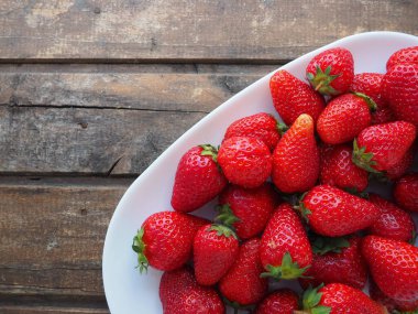 Tabakta çilek, ahşap arka plan. Beyaz tabaklar ve lezzetli kırmızı büyük bahçe çilekleri. Sağlıklı yiyecekler, vitaminler ve vejetaryen diyeti. Yiyeceklerle yaşam. Uzayı kopyala Düz yatıyordu.