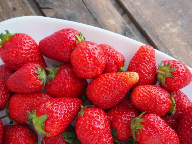 Tabakta çilek, ahşap arka plan. Beyaz tabaklar ve lezzetli kırmızı büyük bahçe çilekleri. Sağlıklı yiyecekler, vitaminler ve vejetaryen diyeti. Yiyeceklerle yaşam. Uzayı kopyala Düz yatıyordu.