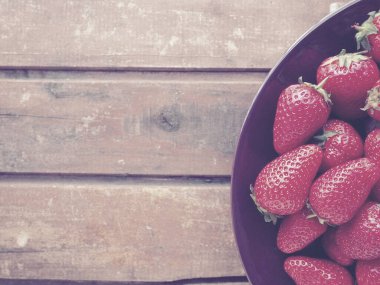 Tabakta çilek, ahşap arka plan. Koyu seramik tabaklar ve lezzetli kırmızı büyük bahçe çilekleri. Sağlıklı yiyecekler, vitaminler ve vejetaryen diyeti. Yiyeceklerle yaşam. Uzayı kopyala Düz yatıyordu