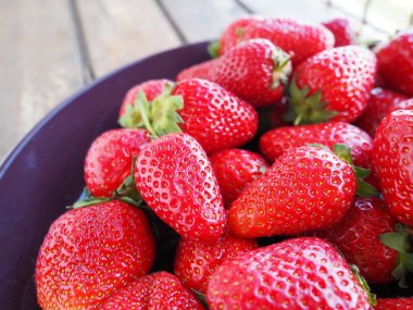 Tabakta çilek, ahşap arka plan. Koyu seramik tabaklar ve lezzetli kırmızı büyük bahçe çilekleri. Sağlıklı yiyecekler, vitaminler ve vejetaryen diyeti. Yiyeceklerle yaşam. Uzayı kopyala Düz yatıyordu