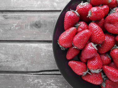 Tabakta çilek, ahşap arka plan. Koyu seramik tabaklar ve lezzetli kırmızı büyük bahçe çilekleri. Sağlıklı yiyecekler, vitaminler ve vejetaryen diyeti. Yiyeceklerle yaşam. Uzayı kopyala Düz yatıyordu