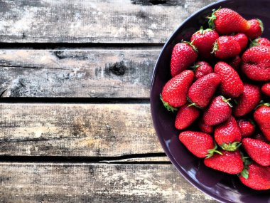 Tabakta çilek, ahşap arka plan. Koyu seramik tabaklar ve lezzetli kırmızı büyük bahçe çilekleri. Sağlıklı yiyecekler, vitaminler ve vejetaryen diyeti. Yiyeceklerle yaşam. Uzayı kopyala Düz yatıyordu