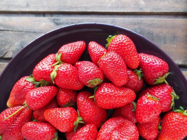 Tabakta çilek, ahşap arka plan. Koyu seramik tabaklar ve lezzetli kırmızı büyük bahçe çilekleri. Sağlıklı yiyecekler, vitaminler ve vejetaryen diyeti. Yiyeceklerle yaşam. Uzayı kopyala Düz yatıyordu