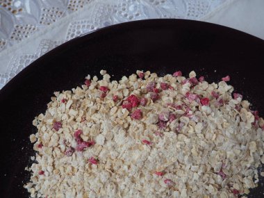 Organic Granola Cereal with oats, powdered sugar and dry raspberries. Healthy muesli as a dry mix. An antidiabetic, low calorie, healthy diet. Black utensils.