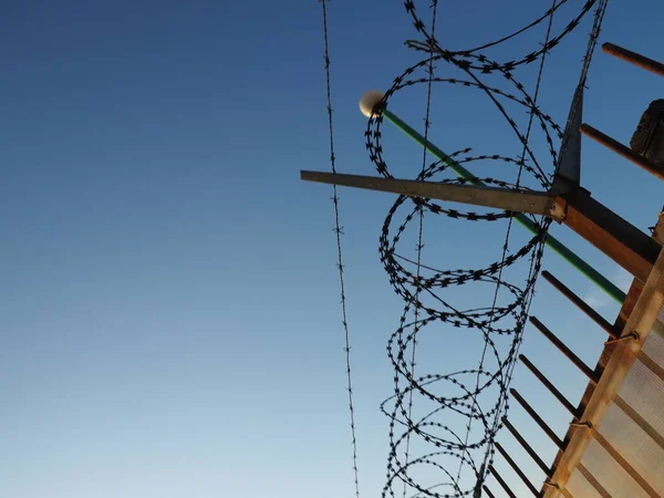 Barbed wire in skeins and stretched against the blue sky. Barbed wire against thieves and vandals. An insurmountable obstacle. Rusty wire, rows, spiral and coils of barbed wire