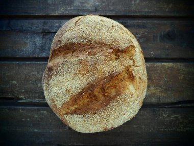 Yuvarlak ekmeğin üst görüntüsü. Eski ahşap bir masaya serpiştirilmiş lezzetli taze mısır ekmeği. Uzayı kopyala Geleneksel tarifler. El yapımı ekmek..