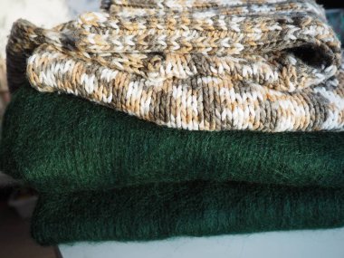 Örgü kıyafetler, gelişigüzel katlanmış. Dalgalı polyester ve yeşil yün kazaklar. Sıcak kışlık giysiler. Örgü tarzı sakız. Yüksek kalite fotoğraf.