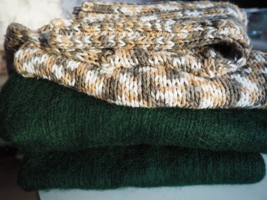 Örgü kıyafetler, gelişigüzel katlanmış. Dalgalı polyester ve yeşil yün kazaklar. Sıcak kışlık giysiler. Örgü tarzı sakız. Yüksek kalite fotoğraf.