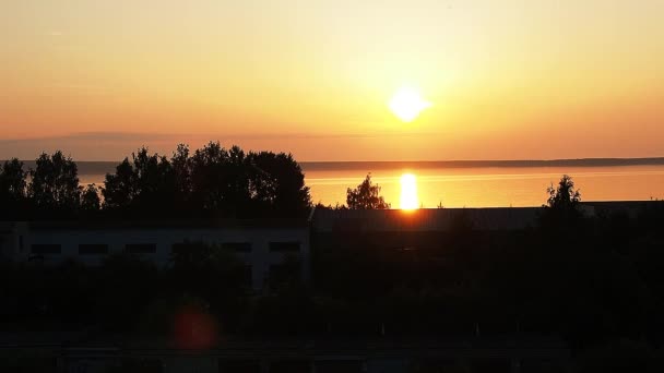Amanecer amarillo-anaranjado y el ascenso del sol sobre el lago Onega en verano. Amanecer y levantar el disco solar de las nubes. Reflejo del sol en el agua. Pista solar en la superficie del agua — Vídeo de stock
