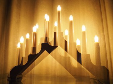 Schwibbogen kemeri, bir şamdan şeklinde parlıyor. Sarı arka plan. Akşam, romantik, şenlikli, dini ya da mistik atmosfer. Mum ışığını andıran yanan ampuller. Çift pozlama.