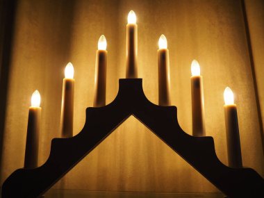 Schwibbogen kemeri, üçgen bir şamdan şeklinde. Sarı arka plan. Akşam, romantik, şenlikli, dini ya da mistik atmosfer. Mum ışığına benzeyen yanan ampuller.