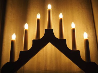 Schwibbogen kemeri, üçgen bir şamdan şeklinde. Sarı arka plan. Akşam, romantik, şenlikli, dini ya da mistik atmosfer. Mum ışığına benzeyen yanan ampuller.