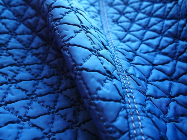 Blue synthetic quilted raincoat fabric close-up. Machine stitches are sewn in several directions to create an effect of volume and structure. Textile industry. Abstract background with gradient.