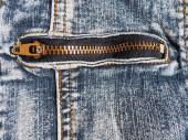 Detailní džíny se švy a zámky. Těžce ošuntělé džíny. Kovový bronzově žlutý zámek s držákem. Kapsa na džínách.