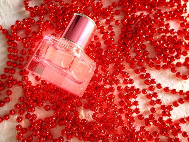 Parlak kırmızı kadın boncuklarının üzerinde altın kapaklı cam bir parfüm şişesi duruyor. Kadın mücevherleri, kozmetik ürünleri ve mücevherler. Kadınsı natürmort hayat. Kapatın. Düz yatıyordu.