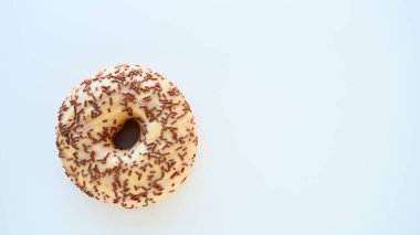 Mavi arka planda donut yakın plan. Vanilya kreması ve çikolata parçacıklarıyla kaplı lezzetli bir pasta. Yüksek kalorili kahvaltı ya da atıştırmalık. Vanilyalı, çikolatalı, çörekli ya da hamurlu lezzetli bir tatlı..