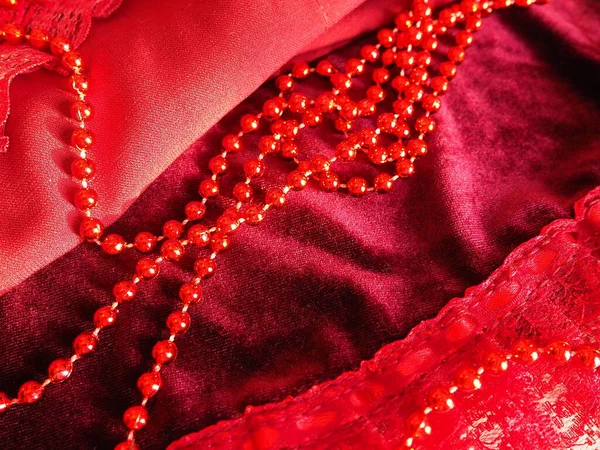Red beautiful beads on bright scarlet velvet. Beautiful luxurious women\'s jewelry on soft fabric. Flat lay close-up. Women\'s stuff and cosmetics. Items as a background. Defocused soft focus.
