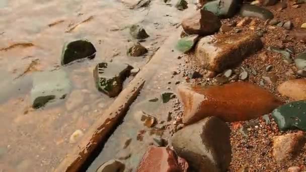 Wasser singt auf Felsen am Ufer eines Sees oder Meeres. Die Welle verläuft am sandig-felsigen Ufer. Abgebrochener hölzerner Ast neben den Steinen. Saynavolok, Onega-See, Karelien. — Stockvideo