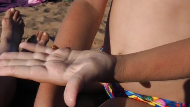 Petrozavodsk, Rusia, 10 de julio de 2021. Una chica en una playa de arena. Un escarabajo mariquita se arrastra en la mano del niño. La chica protege al escarabajo. Insectos en la playa. Ayuda para los animales. Verano playa diversión. — Vídeo de stock