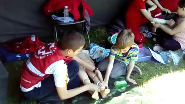 Sremska Mitrovica Serbia 18 mayo 2019 Los niños aprenden a prestar primeros auxilios en caso de lesiones. Ejercicios militares de vendaje. Aplicar un vendaje y un torniquete en las extremidades de un muñeco de plástico. Lesión en la pierna. — Vídeos de Stock