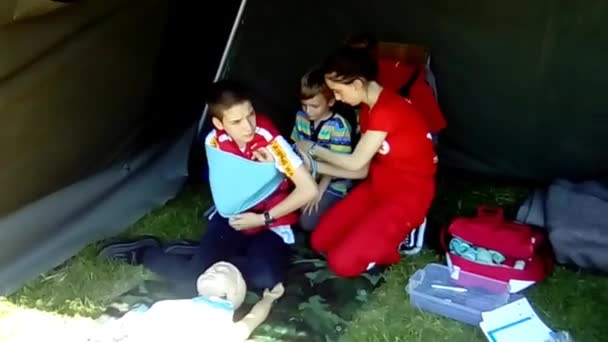 Sremska Mitrovica Serbia 18May 2019 Children learn to put a bandage on a broken arm. First aid in the field in a tent. Training in the camp. The girl ties the boys right hand with a scarf. Arm injury — Stock Video