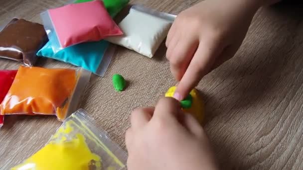 子供の手は柔らかいプラスチックを粉砕します プラスチックのパッケージがテーブルの上にあります 手の細かいモータースキルの開発のための創造性 プラスチック製の金型またはモデルの作成 — ストック動画