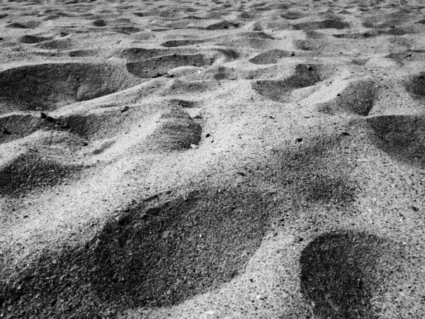 Arena bajo la luz del sol. Playa vacía, huellas y abolladuras en la arena. Dunas del Mar Negro. Roca sedimentaria suelta. granos de montaña y dióxido de silicio de cuarzo mineral. Monocromo blanco-negro. — Foto de Stock