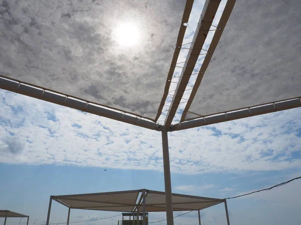 Cobertura de sombreamento feita de vigas de madeira e tecido branco. Aproveite o seu tempo em uma praia de luxo em clima ensolarado protegido contra raios UV. Céu azul, sol e nuvens brancas. Olhando para cima de uma posição deitada. — Fotografia de Stock