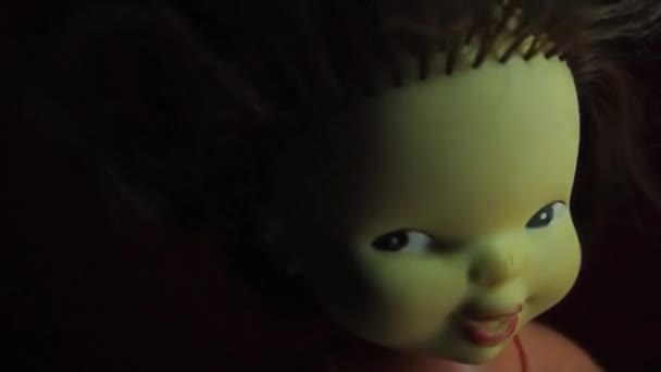 Страшная винтажная кукла с желтым лицом смотрит на зрителя. Луч света качается над головой. Хитрый взгляд, взъерошенные темные волосы и таинственная полуулыбка. Ночь и тьма. Концепция Хэллоуина ужасов — стоковое видео