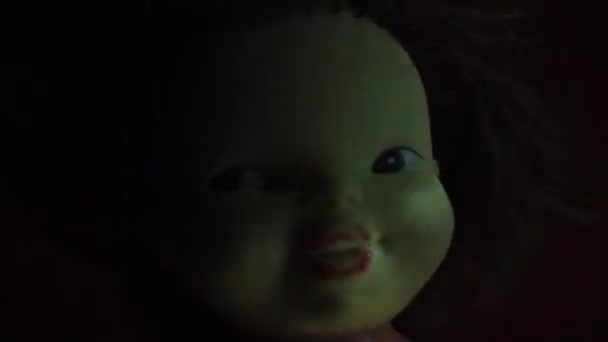 Una muñeca vintage aterradora con una cara amarilla mira al espectador. Un haz de luz se balancea sobre la cabeza. Mirada sosa, pelo oscuro y una misteriosa media sonrisa. Noche y oscuridad. concepto de Halloween horror — Vídeo de stock