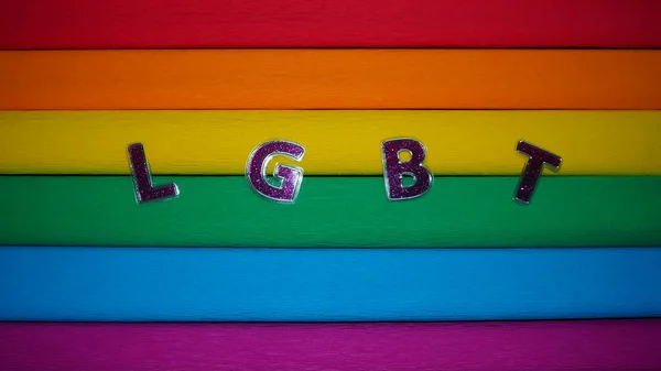 Afkorting LGBT, brief tekst. Paarse LGBT letters op de achtergrond van de regenboogvlag. Donker vignet. Een Rainbow Flag, de Pride Flag. LGBTQ-gemeenschapssymbool. — Stockfoto